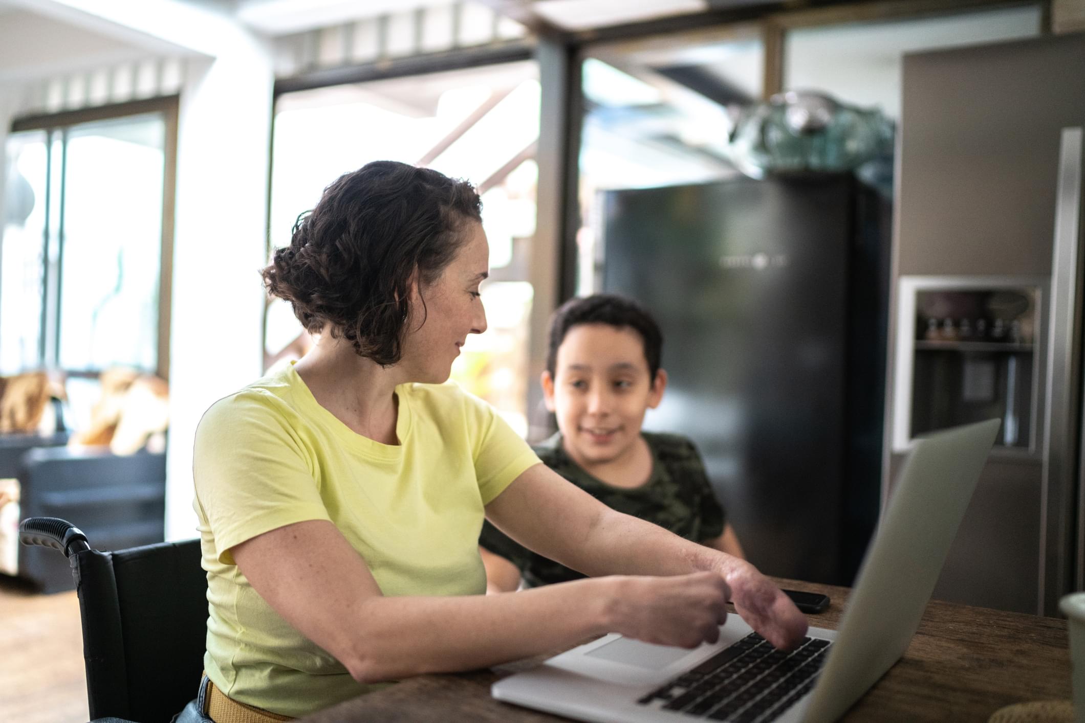 A women sits at a computer helping a young boy.